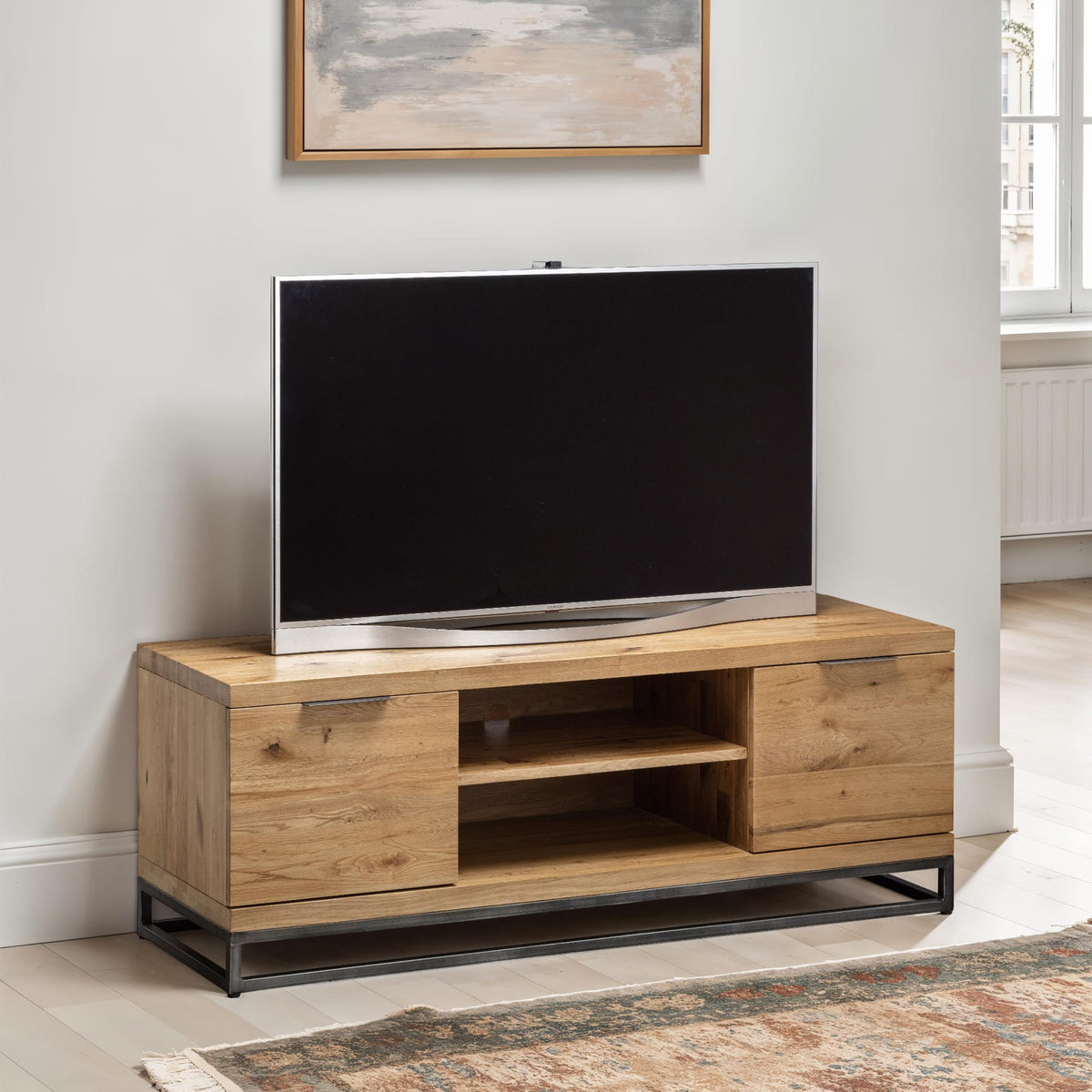 Wooden TV stand with a television on it in a room with a painting on the wall.
