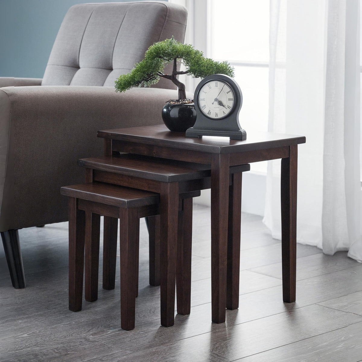 Set of four dark wood nesting tables in a living room setting with a chair and decorative items.