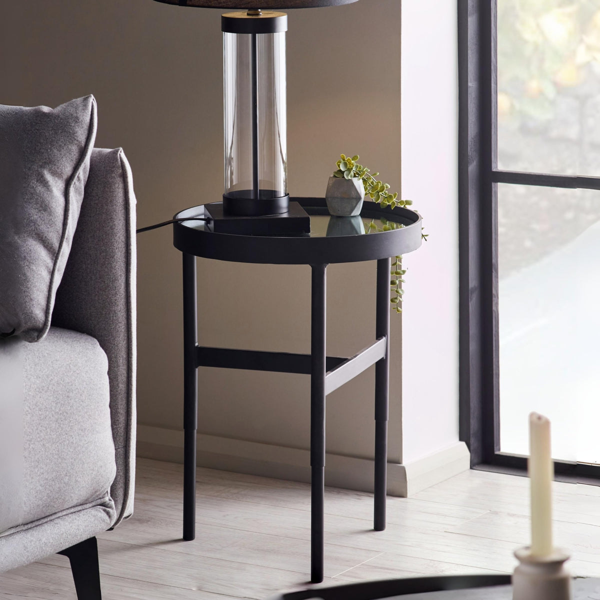 Black side table with a lamp and plant next to a gray sofa in a living room.
