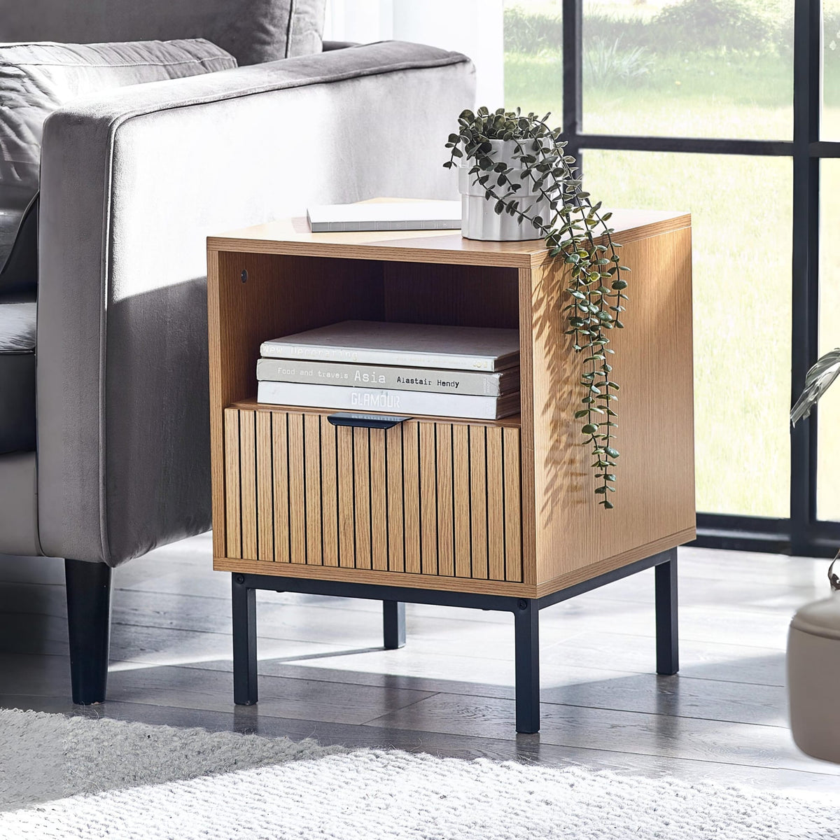 Wooden side table with books and a plant in a living room setting