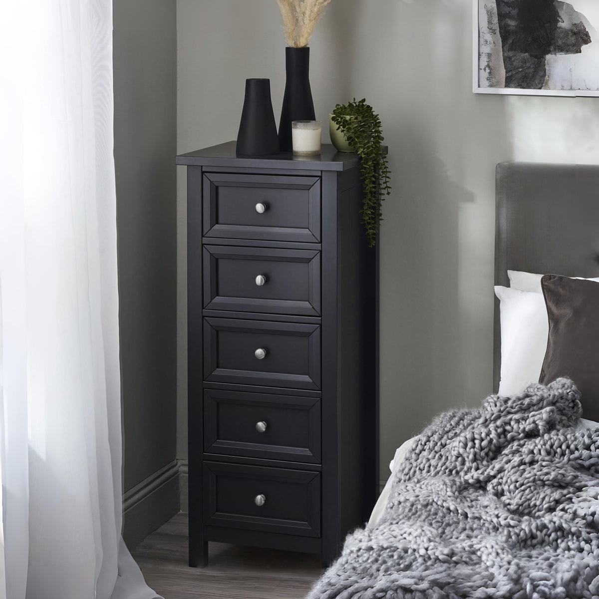 Black tall dresser with decorative items in a bedroom setting