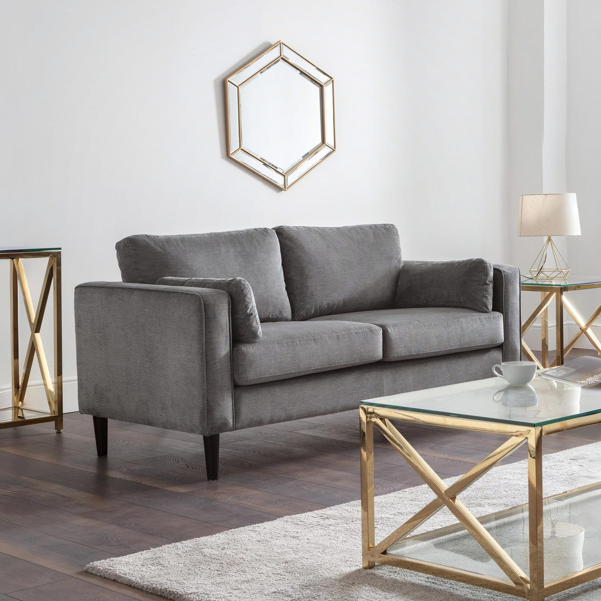 Gray sofa in a modern living room with gold accents and a hexagonal mirror.