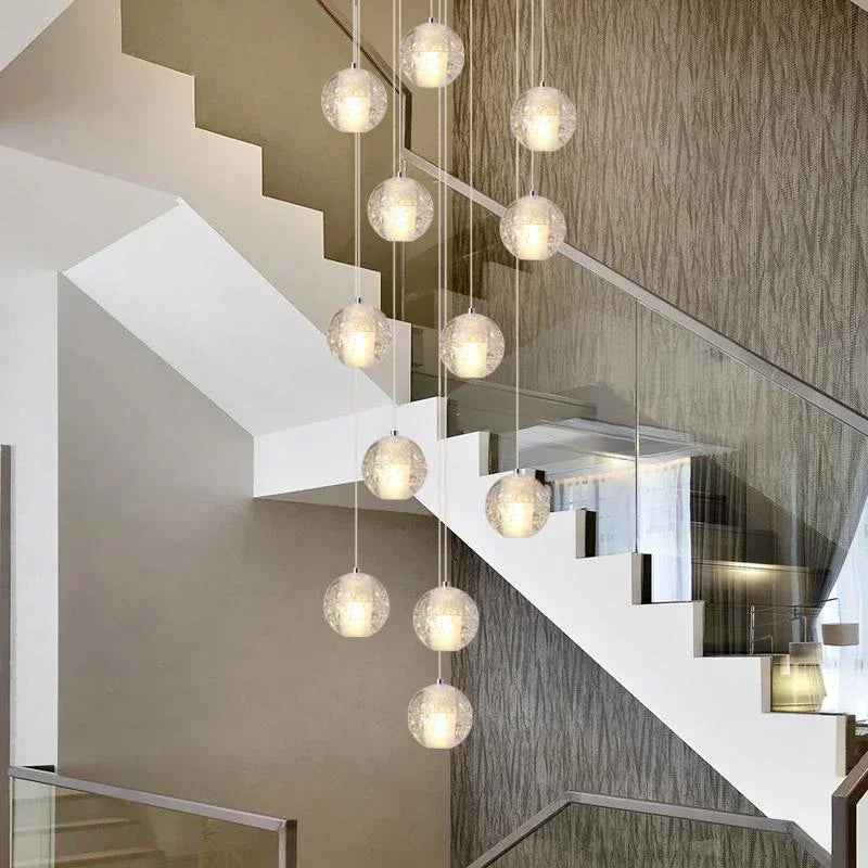 Modern multi-globe crystal pendant light hanging in a tall staircase.