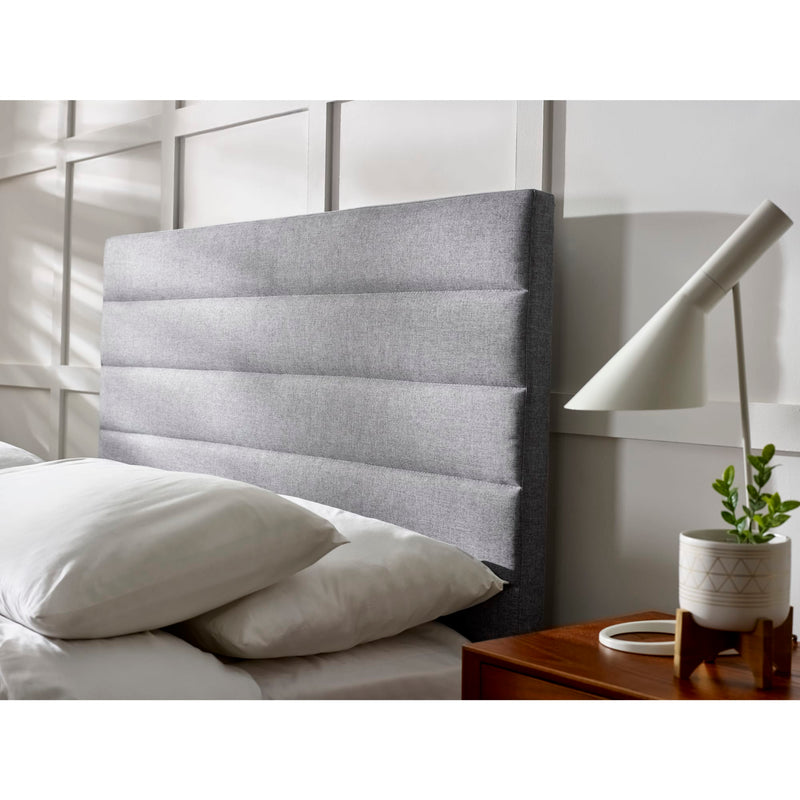Gray upholstered headboard with pillows and a nightstand in a bedroom setting