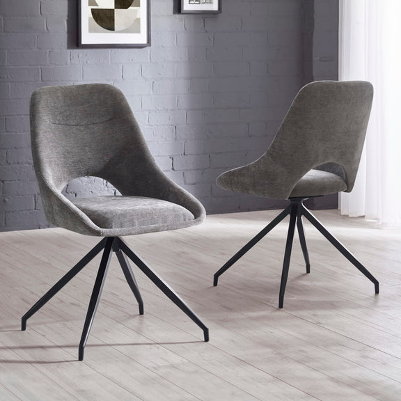 Two gray upholstered chairs with black metal legs on a light wooden floor against a gray brick wall.