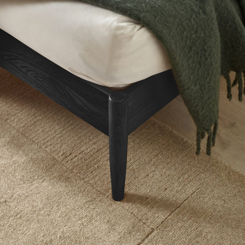 Close-up of a black wooden bed frame with a green blanket on a beige carpet.