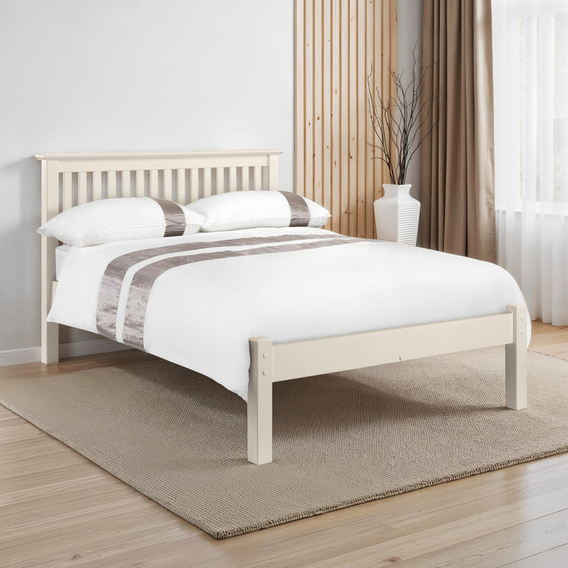 White wooden bed with bedding in a room with curtains and a rug.