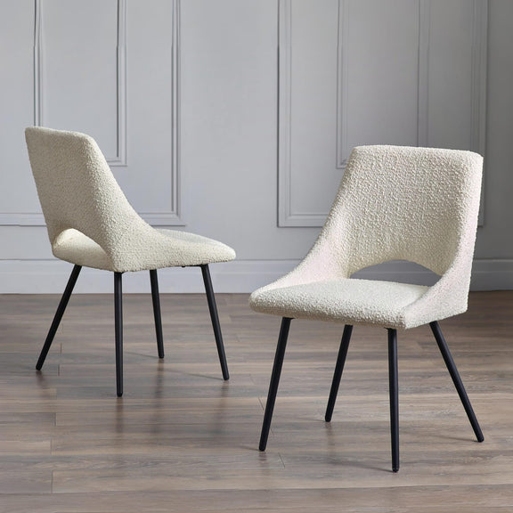 Two beige textured chairs with black legs on a wooden floor against a gray paneled wall.