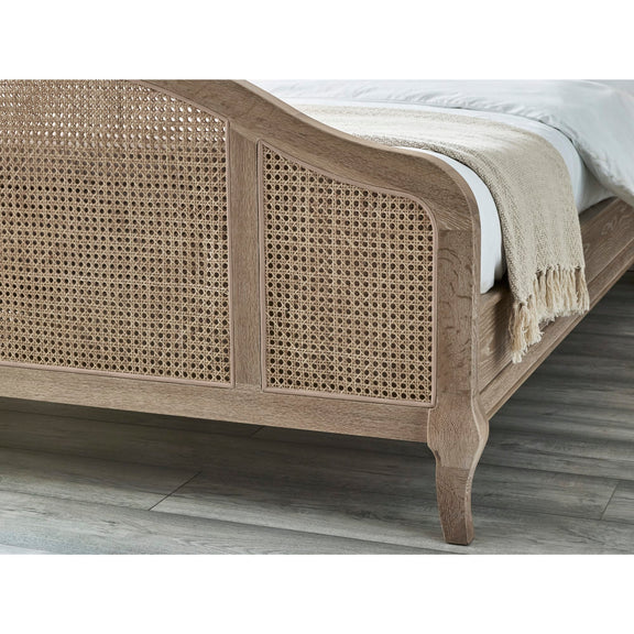 Wooden bed with wicker design and white bedding on a wooden floor.