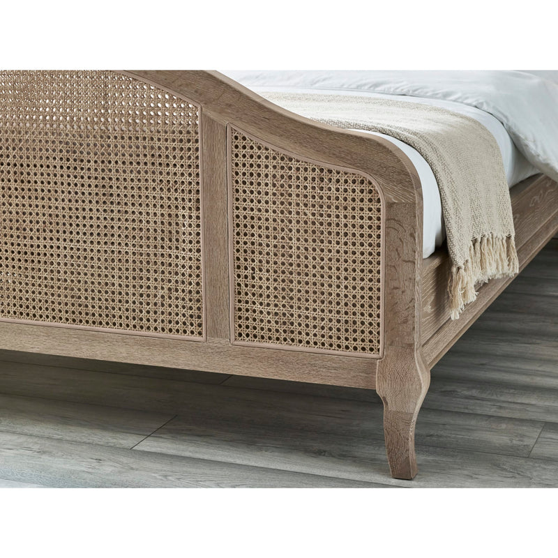 Wooden bed with wicker design and white bedding on a wooden floor.