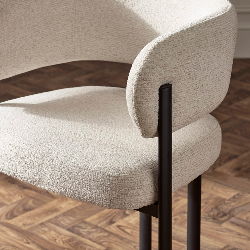 Close-up of a beige upholstered chair with black metal legs on a wooden floor.