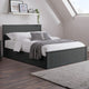 Gray bed frame with white bedding and gray throw in a room with a window and shelf.