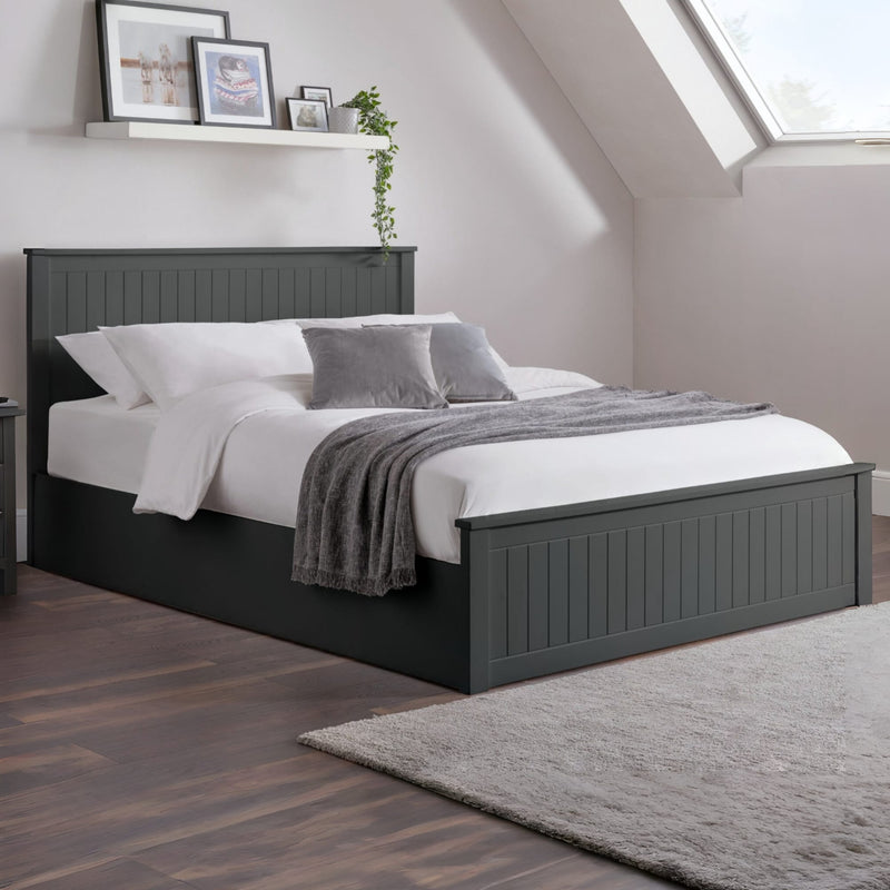 Gray bed frame with white bedding and gray throw in a room with a window and shelf.
