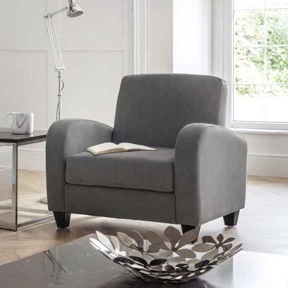 Gray armchair in a living room with a book on it, a lamp, and a decorative bowl.