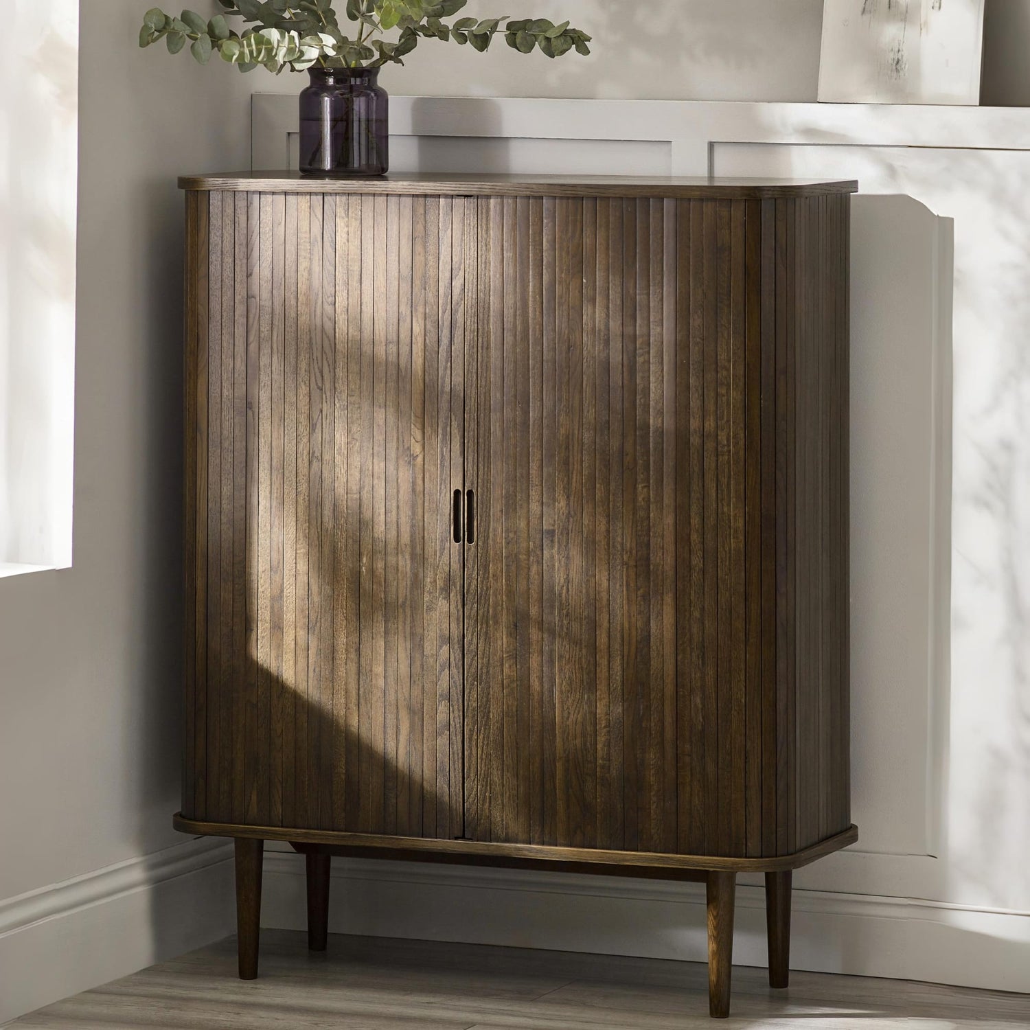 Wooden cabinet with a plant on top in a room with sunlight filtering through.