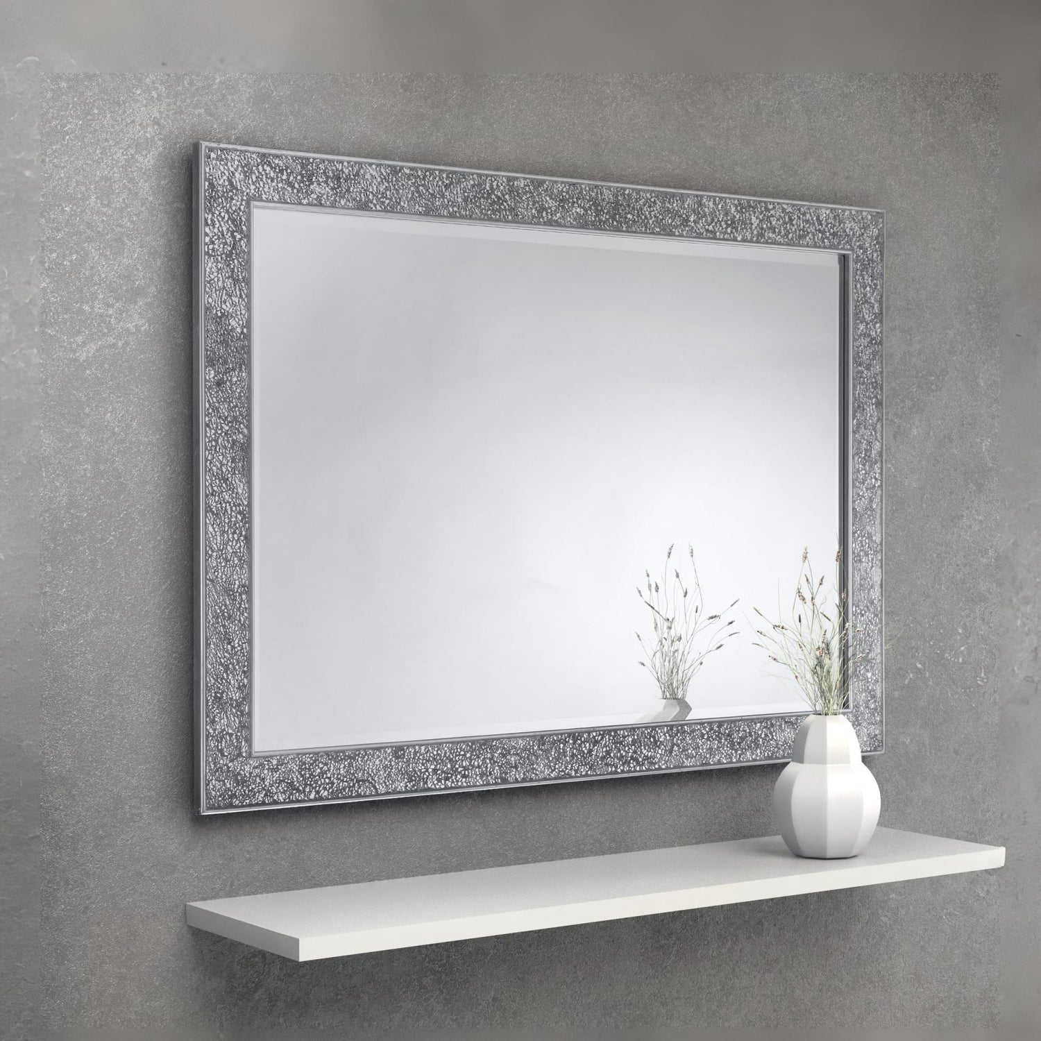 Decorative mirror with a textured frame on a gray wall above a white shelf.