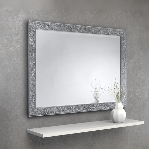 Decorative mirror with a textured frame on a gray wall above a white shelf.