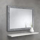 Decorative mirror with a textured frame on a gray wall above a white shelf.