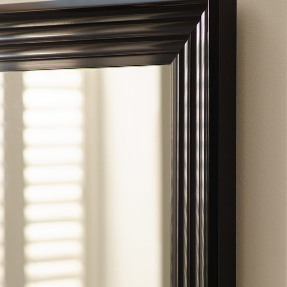 Black framed mirror on a wall with a blurred window in the background