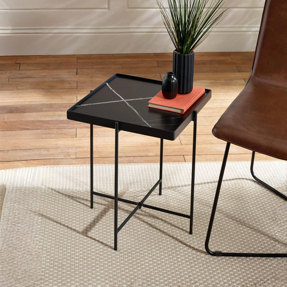 Black marble-patterned side table with a brown chair and decorative items on a wooden floor.