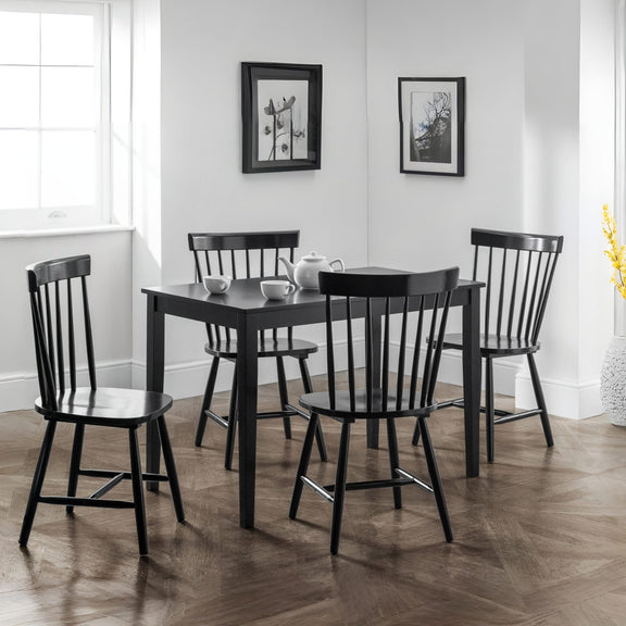 Black dining table with four chairs in a room with white walls and framed pictures.