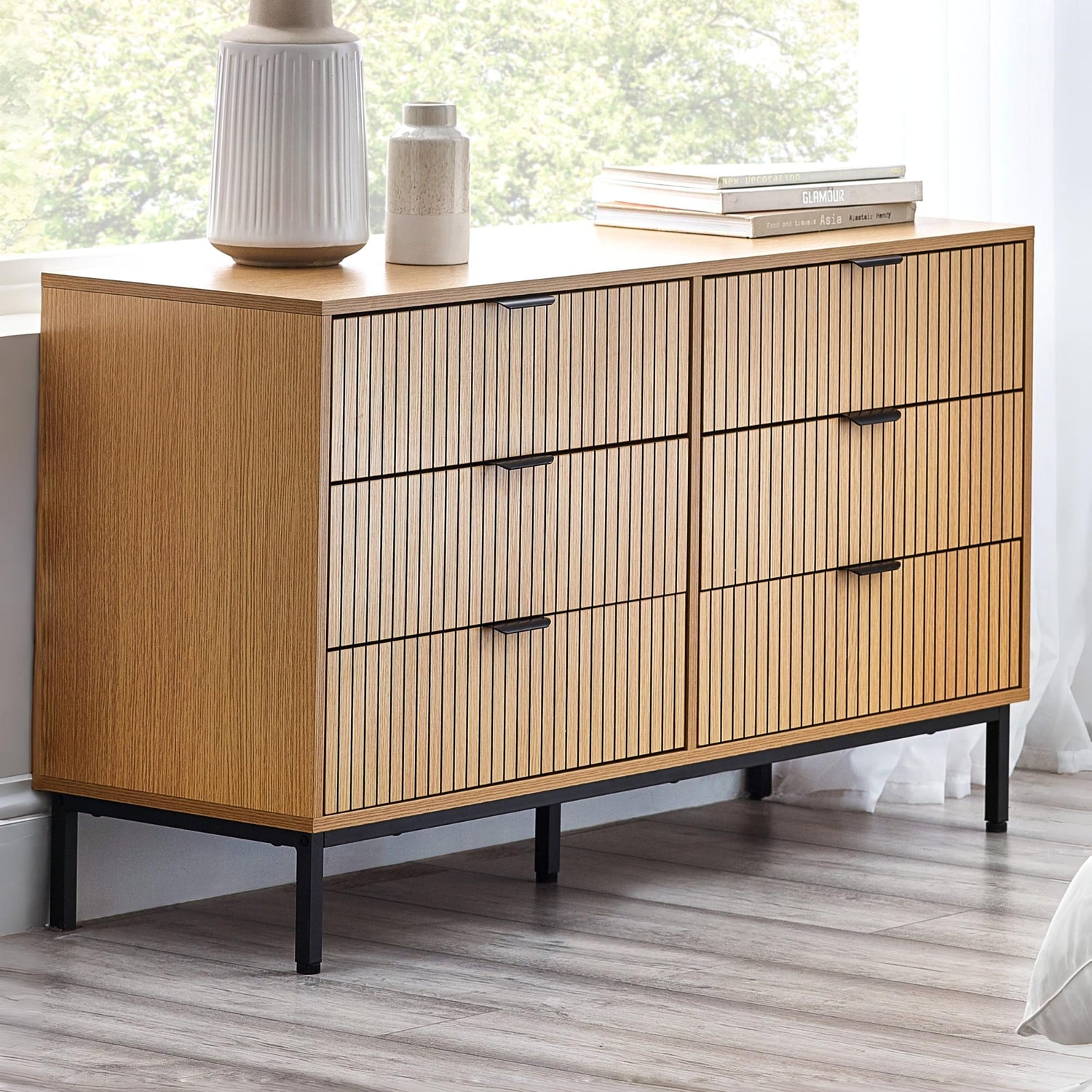 Wooden sideboard with black legs and handles in a room with a window and decor.