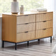 Wooden sideboard with black legs and handles in a room with a window and decor.