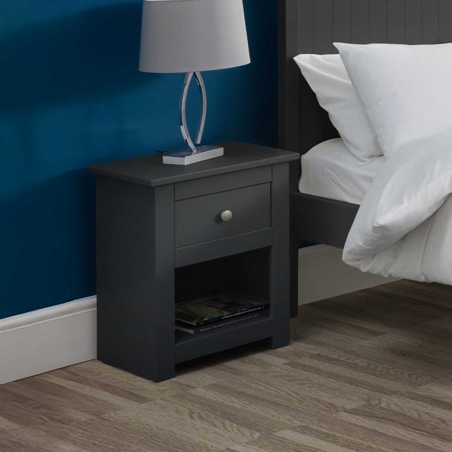 Black nightstand with a lamp next to a bed in a bedroom setting.