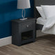 Black nightstand with a lamp next to a bed in a bedroom setting.
