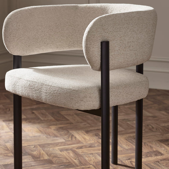 Beige upholstered chair with black metal legs on a wooden floor.