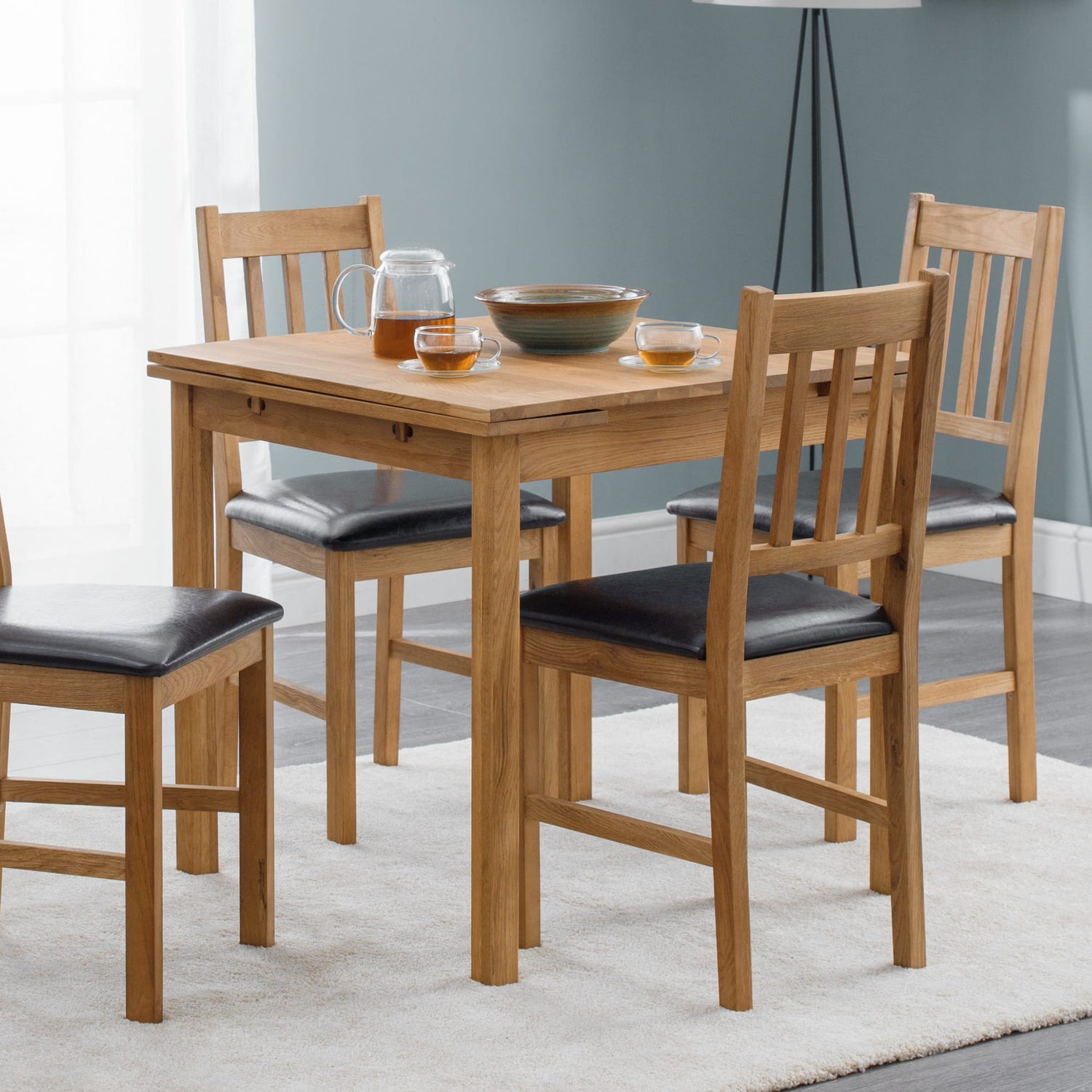 Wooden dining table with four chairs in a room with a gray wall and white curtains.