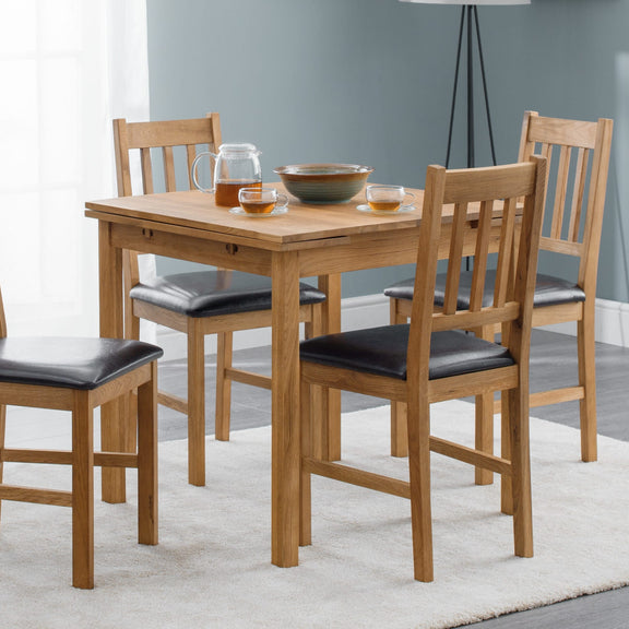 Wooden dining table with four chairs in a room with a gray wall and white curtains.