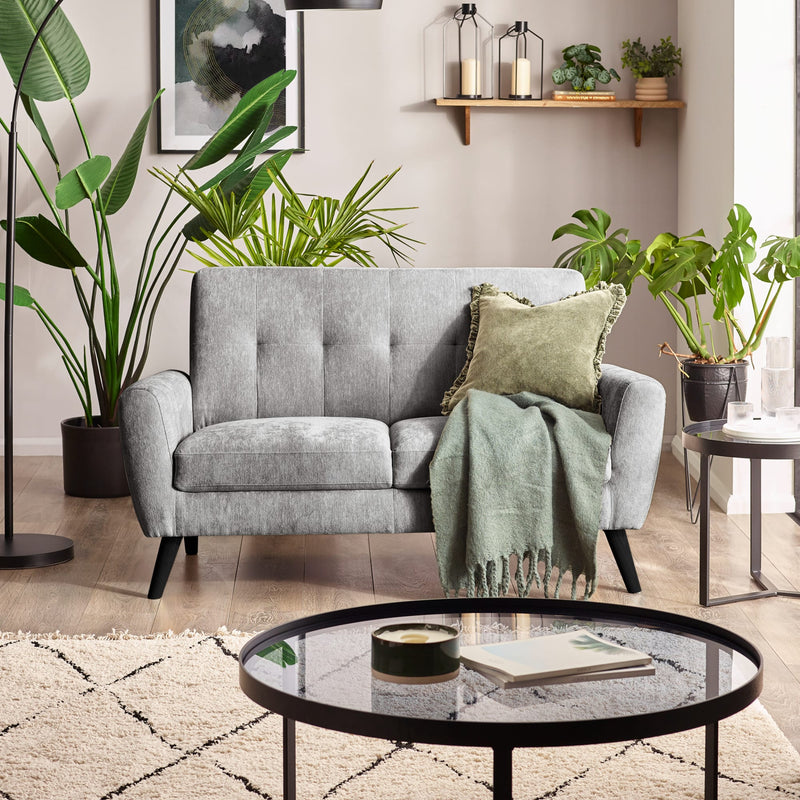 Living room with a gray sofa, green cushions, and a round glass coffee table.
