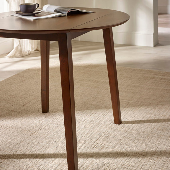 Wooden dining table with a cup and magazine on a carpeted floor