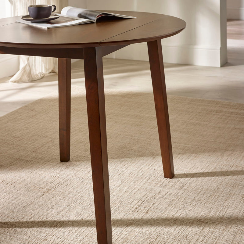 Wooden dining table with a cup and magazine on a carpeted floor