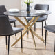Dining table with glass top and gold metal legs, surrounded by gray chairs on a wooden floor.