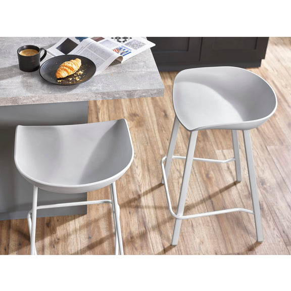 Two white bar stools in front of a table with a cup and plate on a wooden floor.