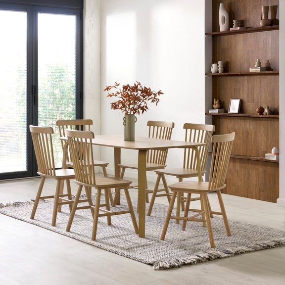 Dining room with wooden table and chairs, rug, and shelves.