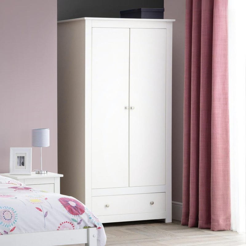 White wardrobe in a bedroom with pink curtains and a bed.