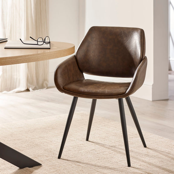 Brown leather chair with black metal legs in a room with a desk and curtains.