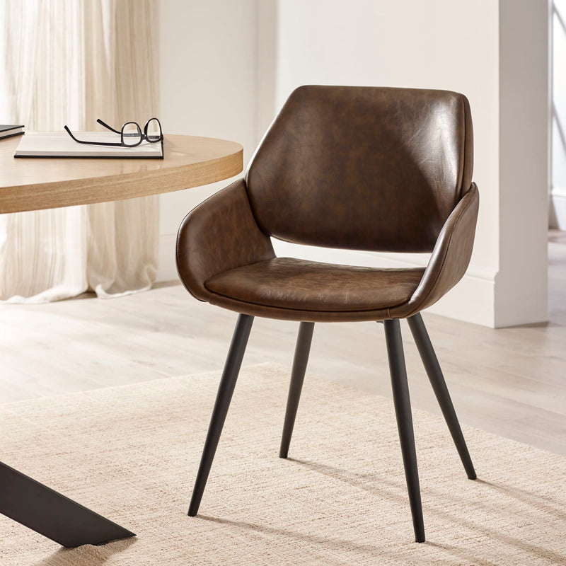 Brown leather chair with black metal legs in a room with a desk and curtains.