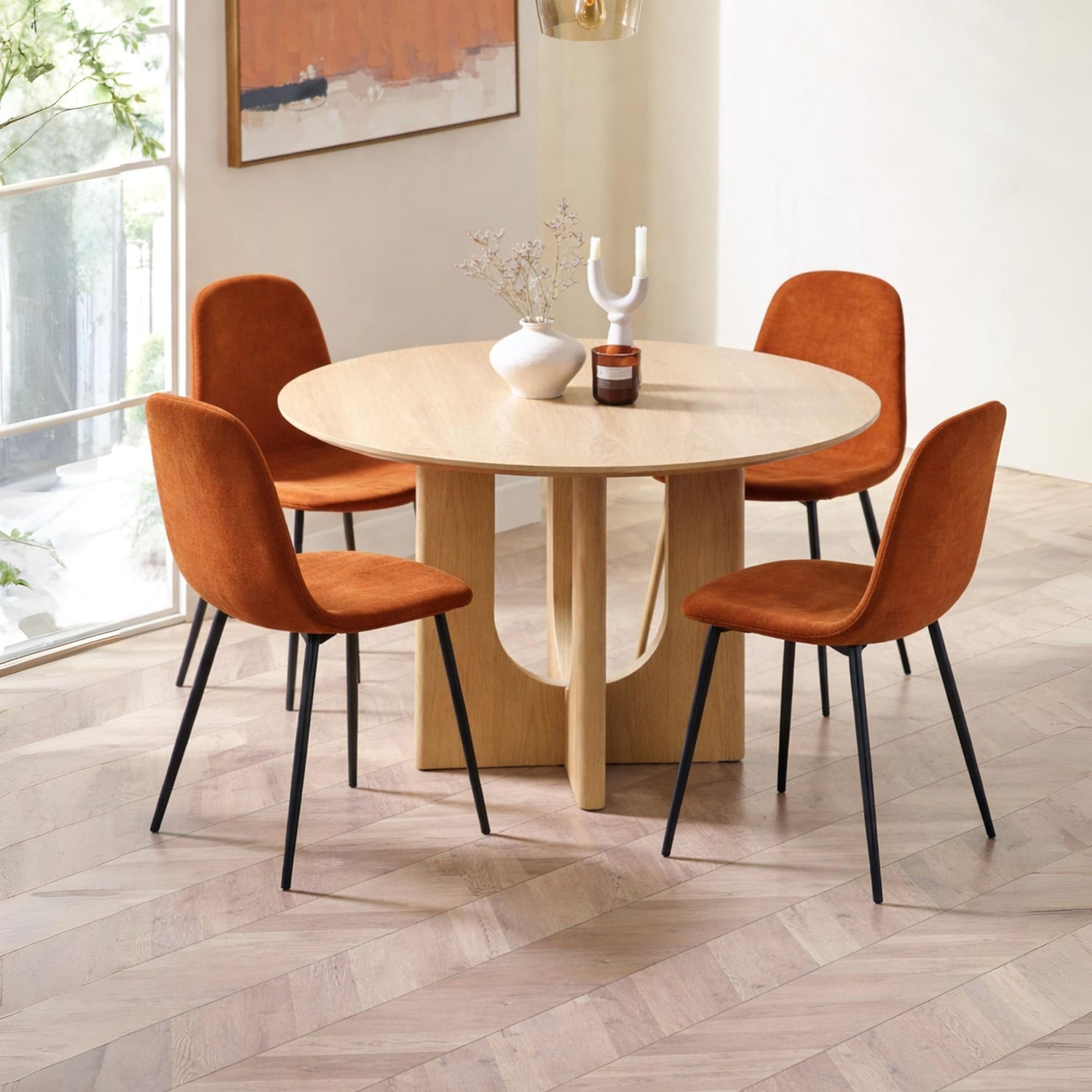Round dining table with four orange chairs in a bright room.