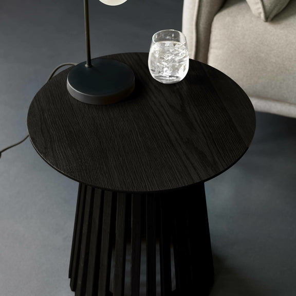 Round black side table with a lamp and glass on a gray floor.