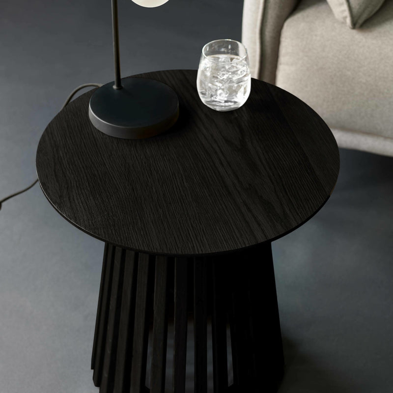 Round black side table with a lamp and glass on a gray floor.