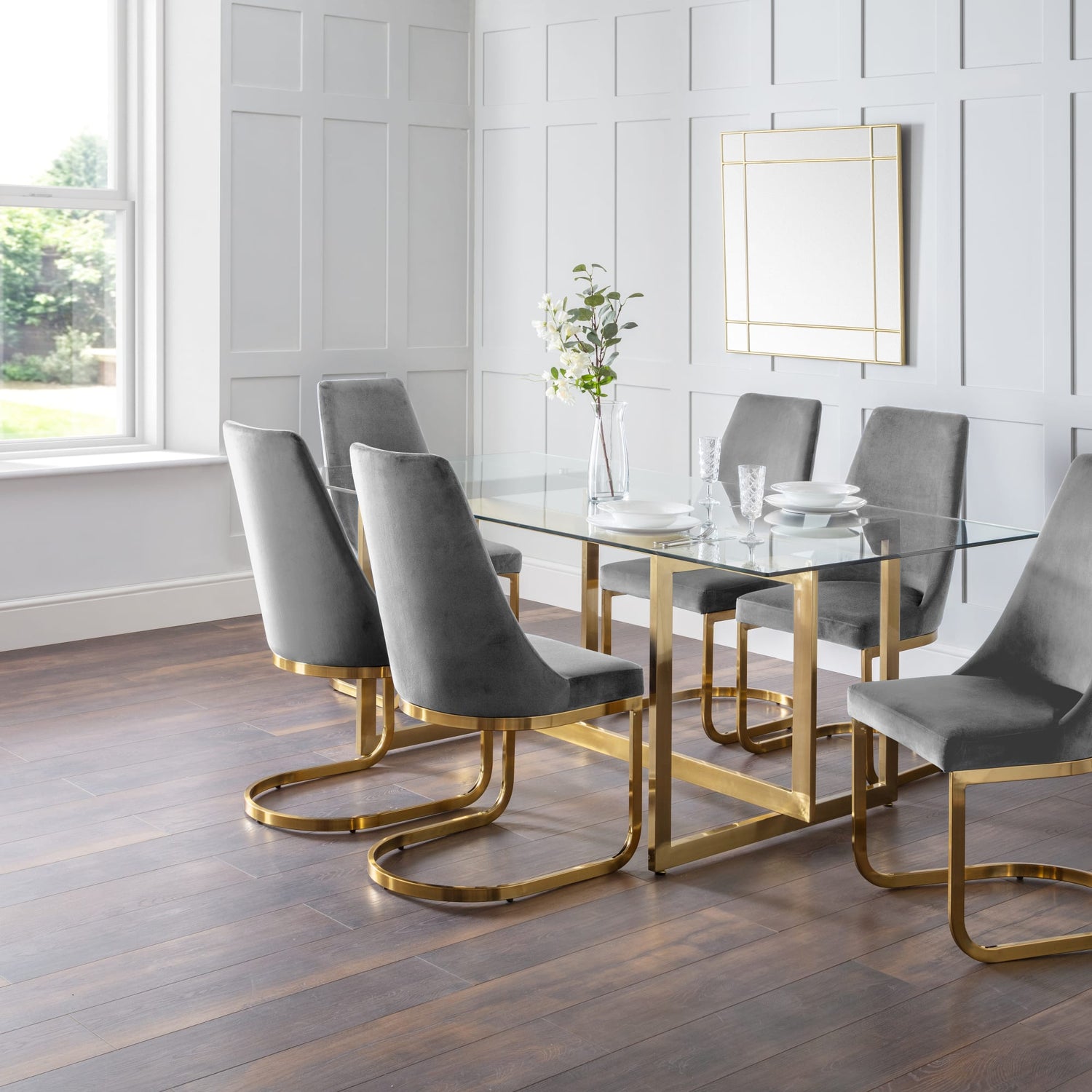Dining room with a glass table and gray chairs on a wooden floor.