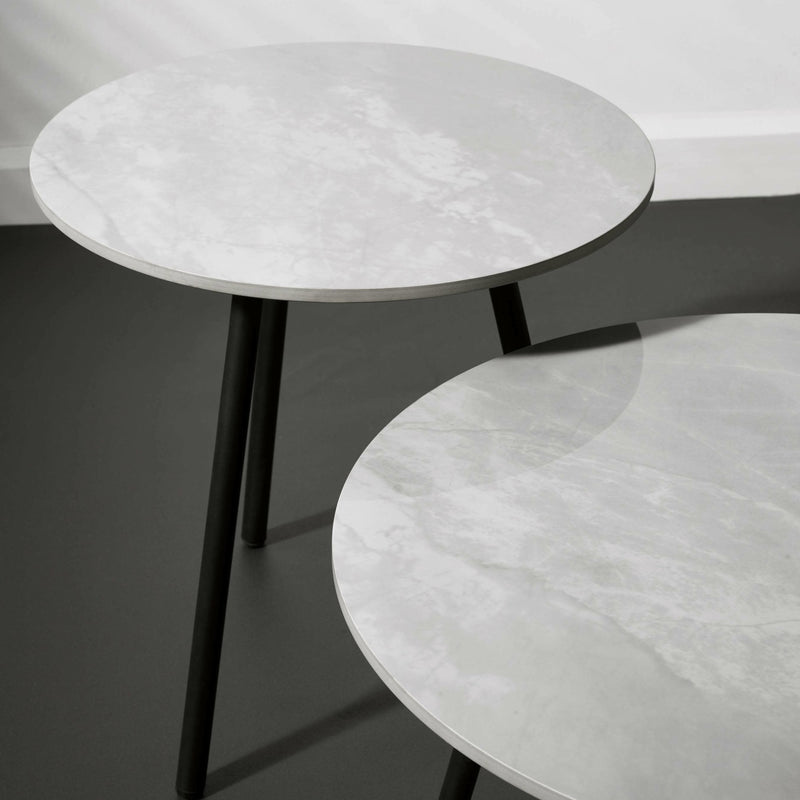 Two round side tables with marble-like tops and black legs on a dark surface.