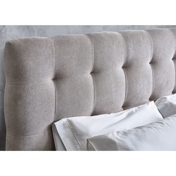 Gray tufted headboard with white bedding against a light gray wall.