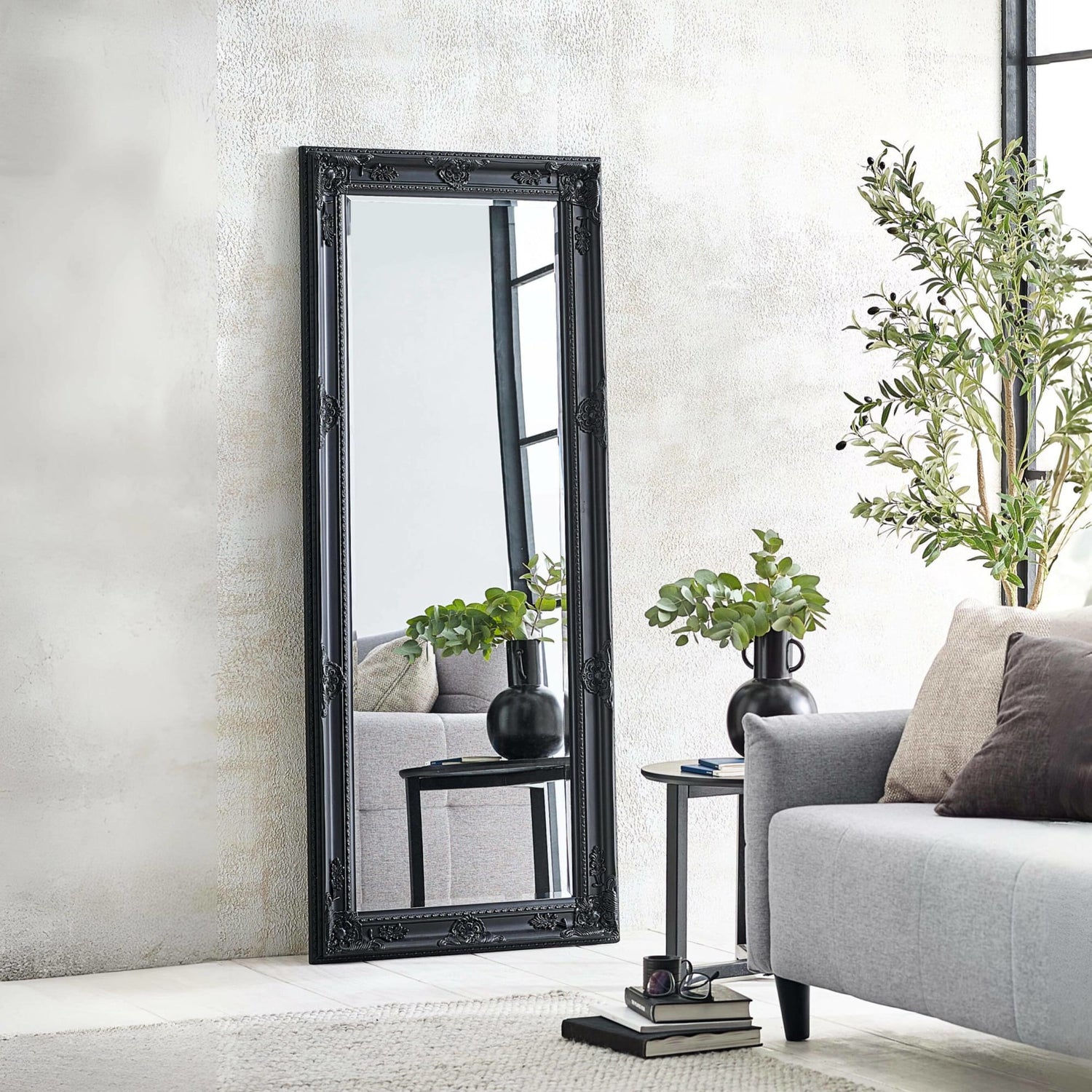 Black decorative mirror leaning against a wall in a living room setting.