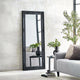 Black decorative mirror leaning against a wall in a living room setting.