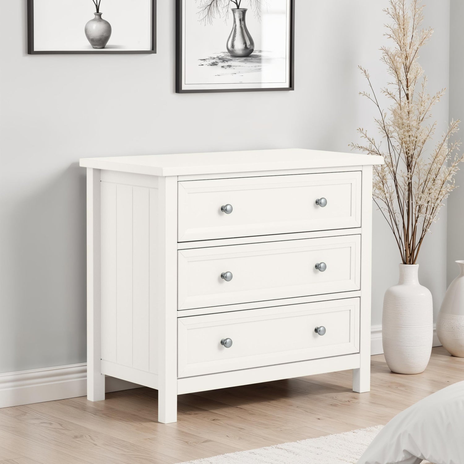 White dresser with three drawers in a room with framed pictures and decorative vases.